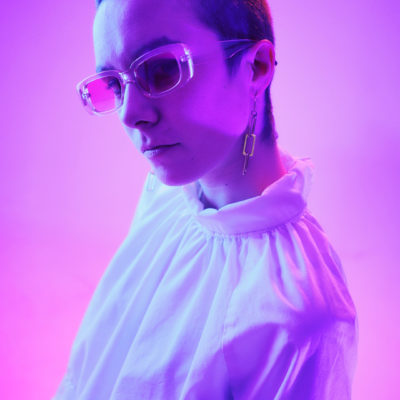 Shauna washed in pink light wearing translucent sunglasses and a white blouse